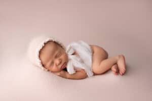 A newborn baby sleeping on a pink background.