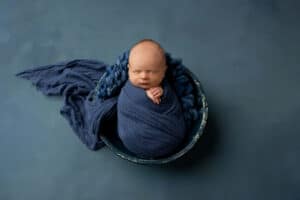 A newborn boy wrapped in a blue blanket on a blue background.