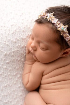 A baby girl wearing a headband and sleeping on a blanket.