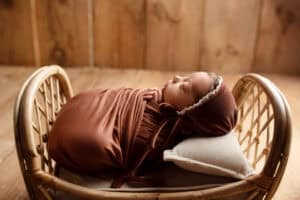 A newborn baby in a brown wrap in a wicker basket.