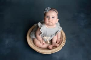 A baby girl sitting in a wooden bowl on a blue background.