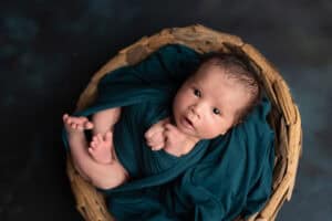 A newborn baby boy in a basket on a dark background.