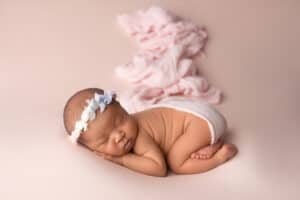 A newborn sleeping on a pink background.