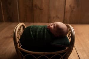 A baby sleeping in a basket on a wooden floor.