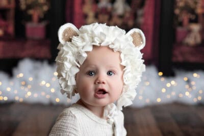 A baby wearing a lion hat in front of a christmas tree.