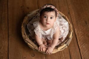 A baby girl sitting in a basket on a wooden floor.