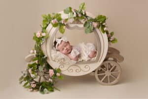 A baby girl is laying in a carriage with flowers.
