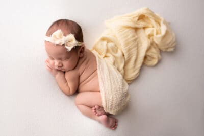 A baby girl wrapped in a yellow blanket sleeping on a white background.