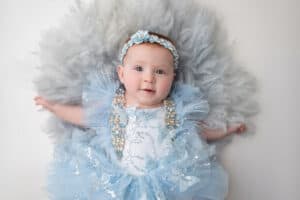 A baby in a blue dress laying on top of feathers.