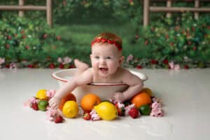 A baby is playing in a bowl of fruit.