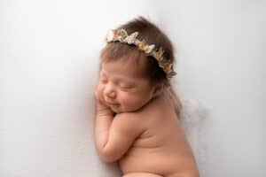 A baby girl wearing a gold crown is laying on a white wall.