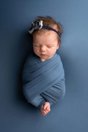 A newborn girl wrapped in a blue wrap on a blue background.