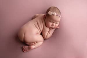 A baby girl sleeping on a pink background.