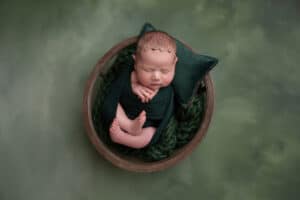 A baby girl is laying in a bowl on a green background.