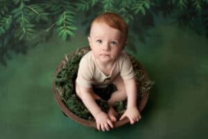 A baby sitting in a wooden bowl on a green background.