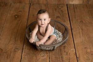 A baby sitting in a basket on a wooden floor.