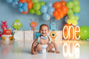 A baby boy is sitting in front of balloons for his first birthday.