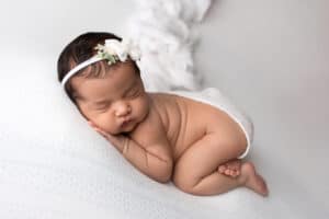 A newborn sleeping on a white blanket with a flower headband.