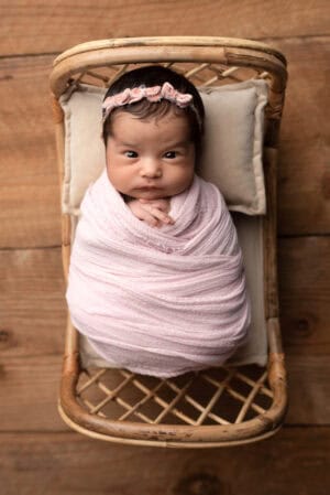 A newborn wrapped in a pink blanket in a wicker basket.