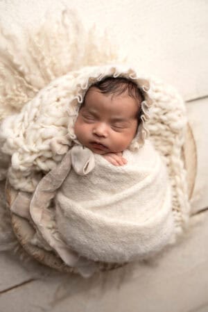 A newborn baby girl wrapped in a blanket on a wooden floor.