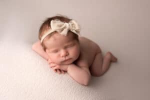 A baby girl is laying on a blanket with a bow on her head.