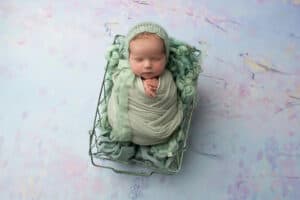 A newborn baby sleeping in a basket on a blue background.