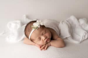 A newborn girl laying on a white blanket.