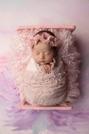 A newborn sleeping in a pink basket on a pink background.