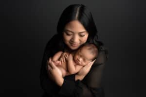 A mother holding her newborn baby on a black background.