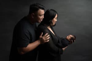 A man and woman holding a baby in front of a black background.