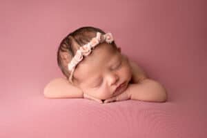 A newborn girl sleeping on a pink background.