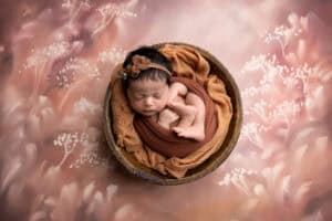 A newborn girl is sleeping in a wooden bowl on a pink background.