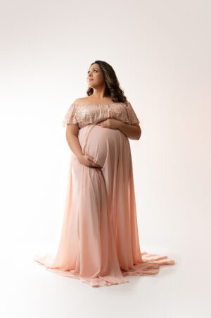 A pregnant woman in a pink dress posing for a photo.