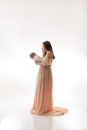 A woman in a peach dress holding a baby in her arms.
