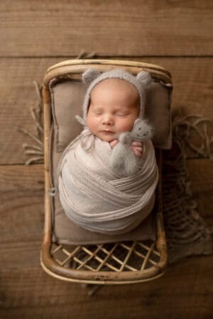 A newborn baby in a wicker basket with a teddy bear.