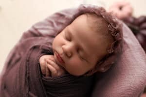 A newborn girl is wrapped in a purple blanket.