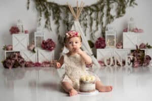 A baby girl sitting in front of a cake in front of a teepee.