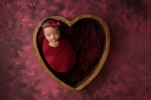 A baby girl is laying in a heart shaped box.