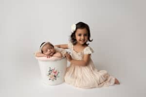 Two newborn girls posing in a bucket on a white background.