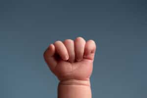 A baby's hand with a fist up on a blue background.