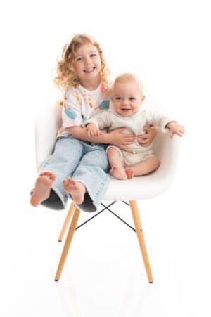 Two children sitting in a white chair on a white background.