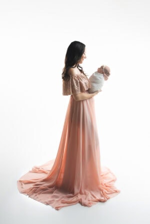 A woman in a pink dress holding her newborn.