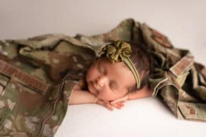A baby girl laying on top of a camouflage blanket.