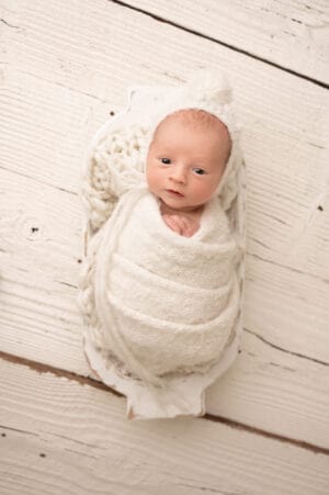 A newborn wrapped in a white blanket on a wooden table.