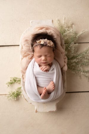 A newborn girl wrapped in a white blanket on a wooden table.