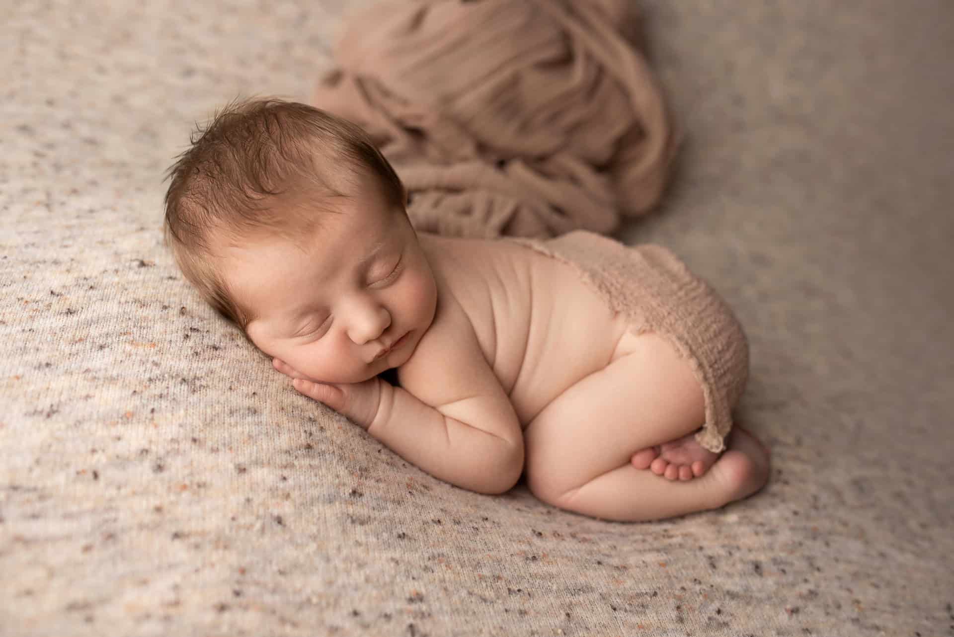 A newborn baby sleeping on a brown blanket.