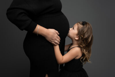 A pregnant woman kisses her daughter's belly.