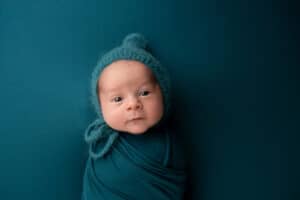 A baby boy in a blue swaddle posing in front of a blue background.