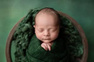 A baby boy wrapped in a green blanket in a wooden bowl.