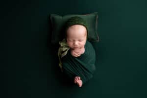 A newborn baby wrapped in a green blanket on a green background.